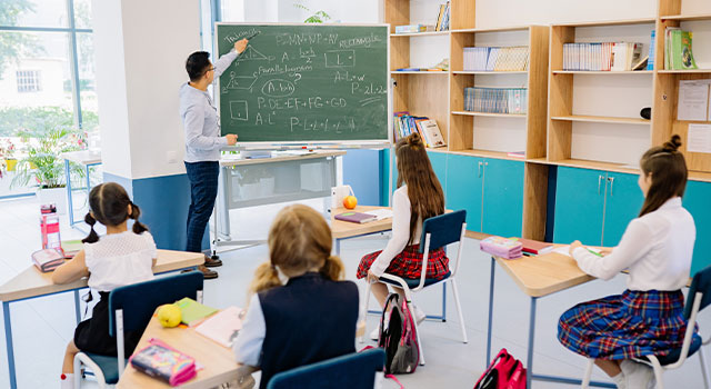 Teacher teaching a class and writing on a board with chalk